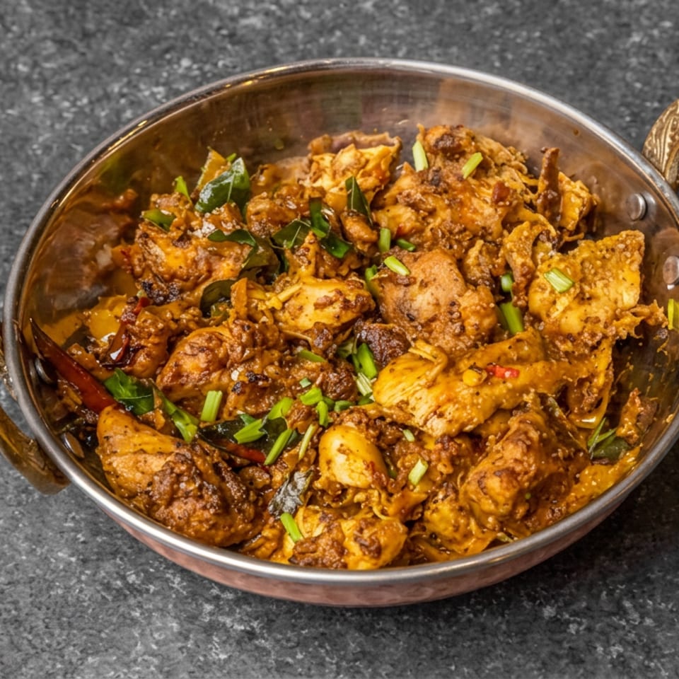 Spiced golden chicken pieces garnished with chopped green onions and herbs in a handled metal serving bowl.